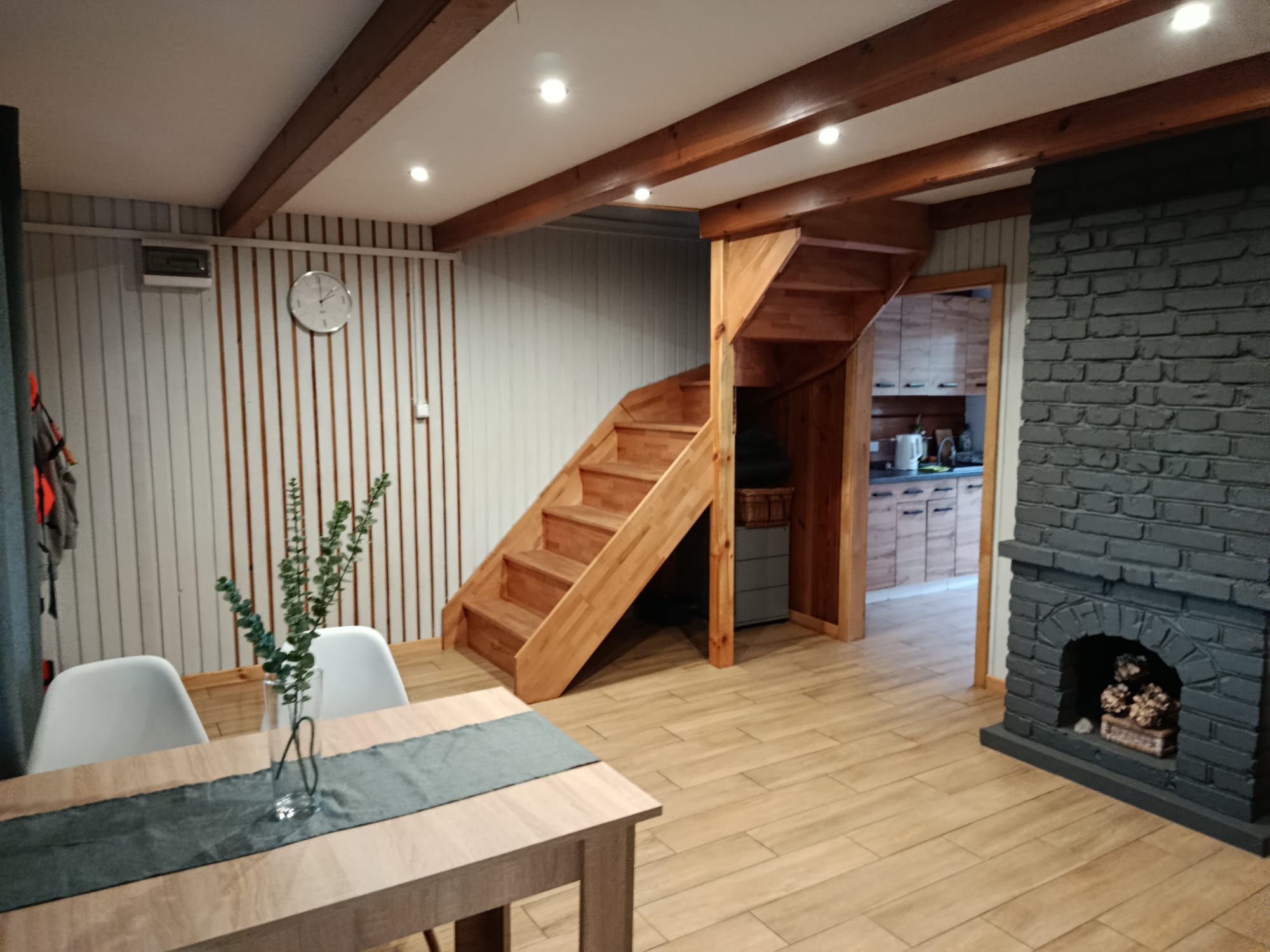 Wnętrze domku letniskowego z kominkiem, schodami drewnianymi i wejściem do kuchni.