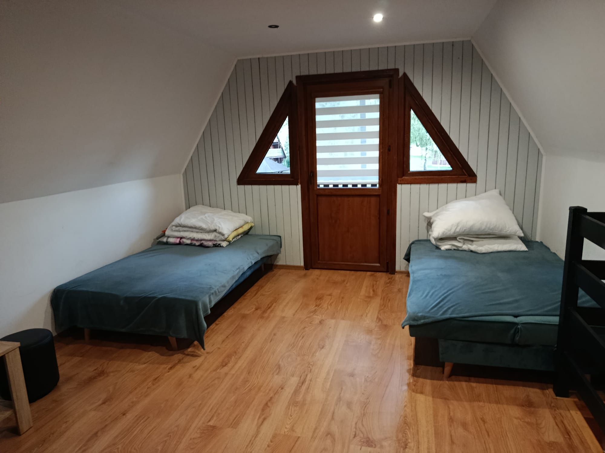 Pokój na piętrze w domku letniskowym z dwoma pojedynczymi łóżkami i wyjściem na balkon.