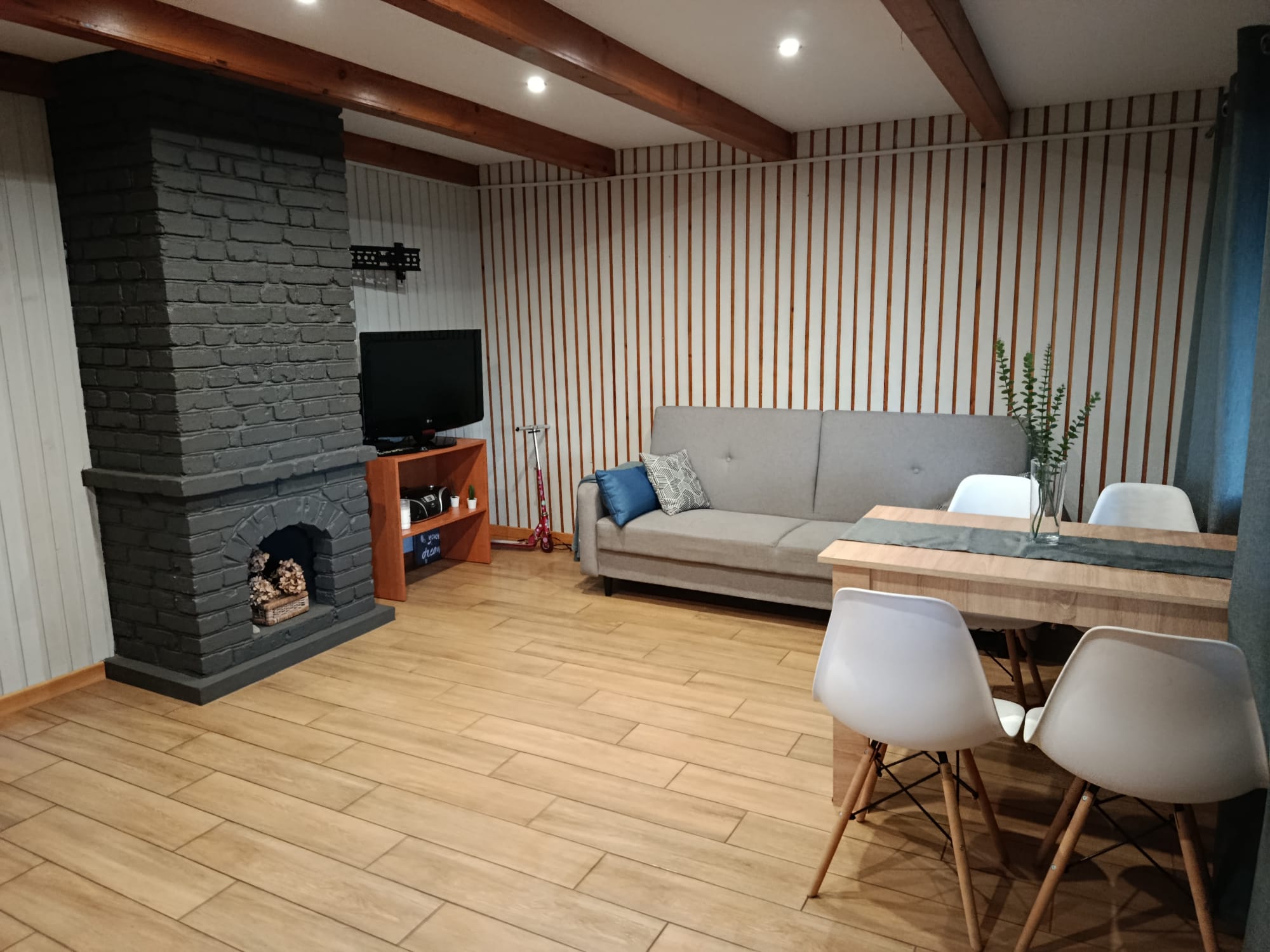 Przytulny salon z kominkiem, sofą i telewizorem w drewnianym domku letniskowym.