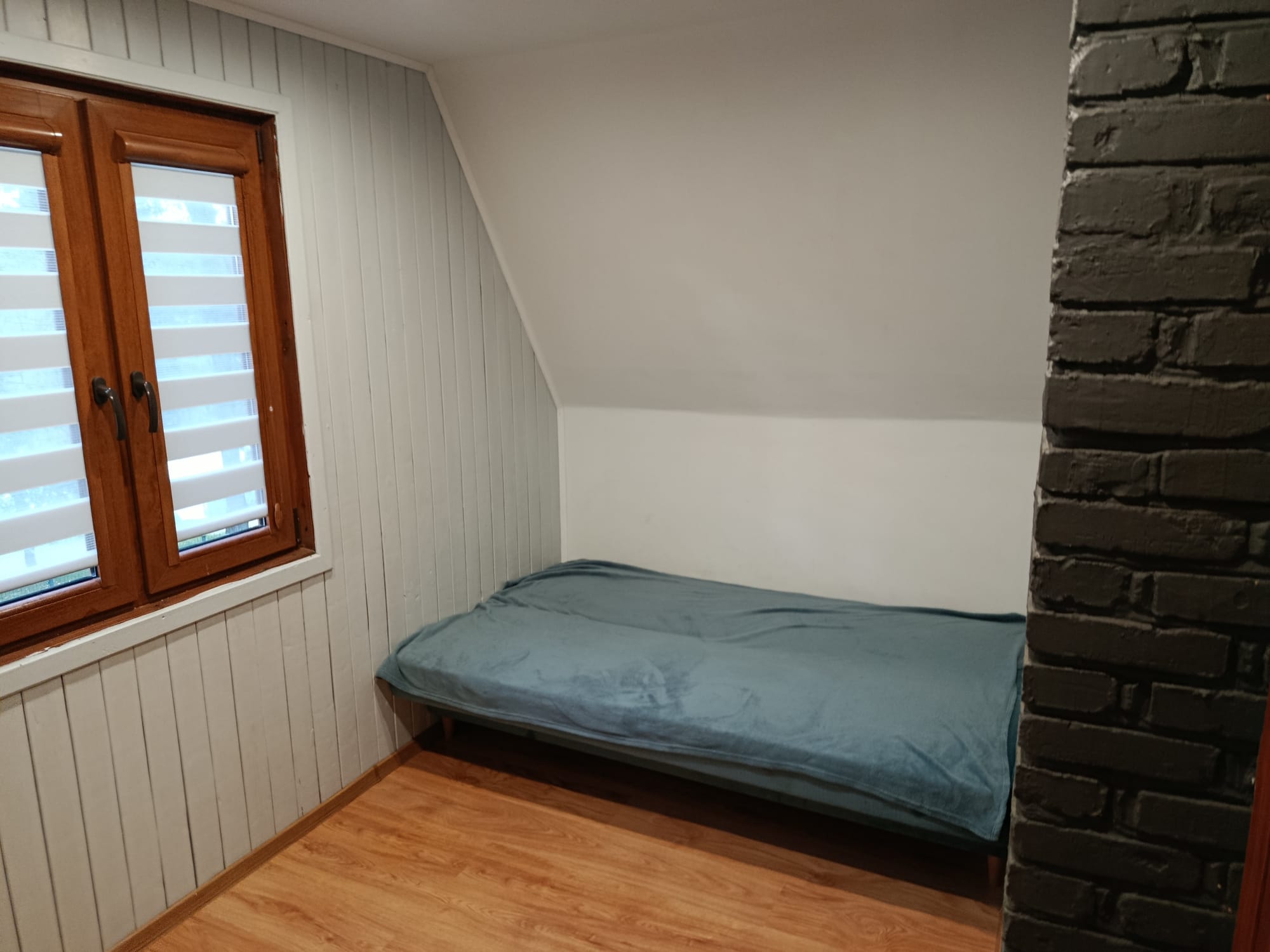 Mały pokój z pojedynczym łóżkiem i oknem, wykończony w jasnym drewnie.