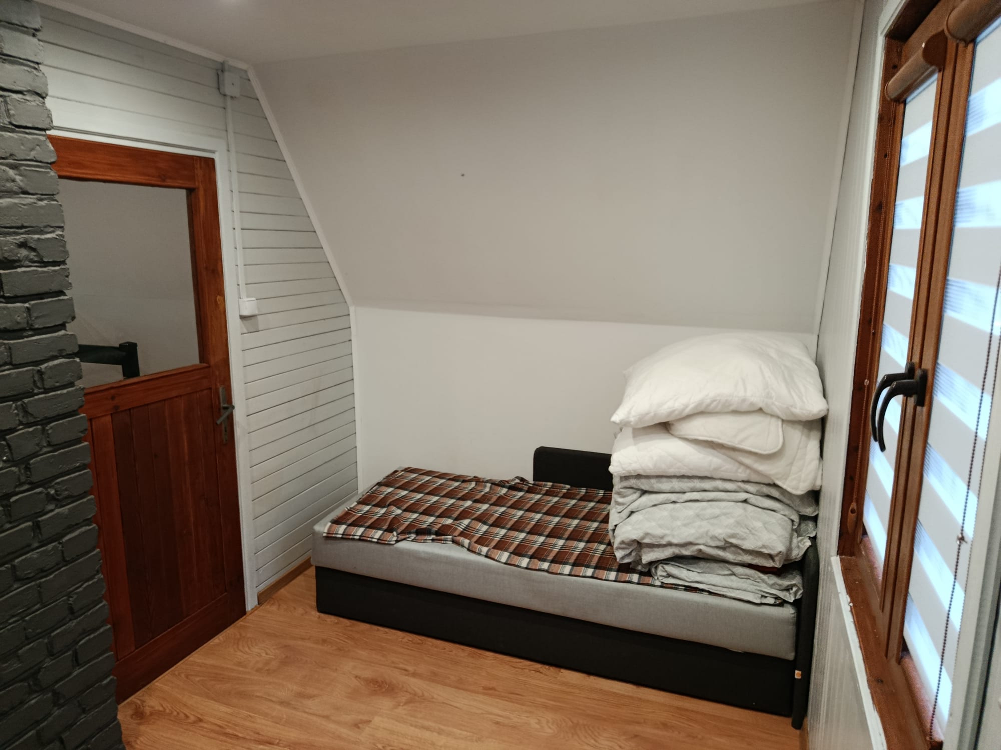 Pokój z łóżkiem, pościelą i drewnianymi drzwiami prowadzącymi do korytarza.