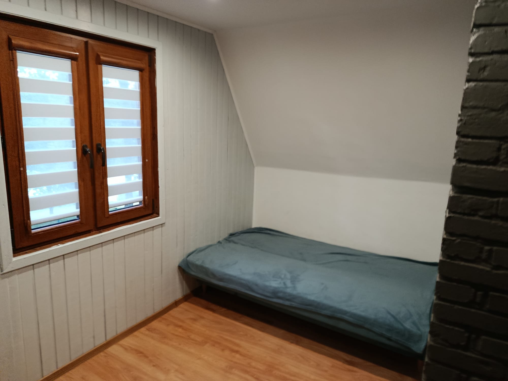 Przytulny pokój z pojedynczym łóżkiem i oknem z roletami w domku letniskowym.