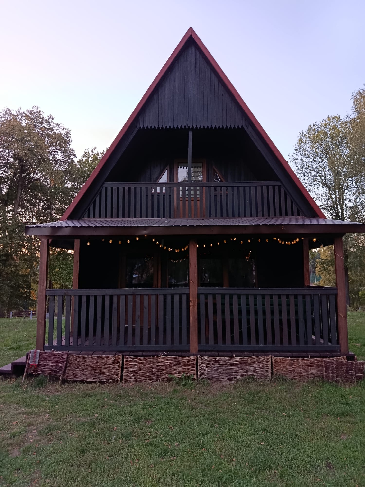 Domek letniskowy z dużym zadaszonym tarasem i balkonem na piętrze, oświetlony girlandami.